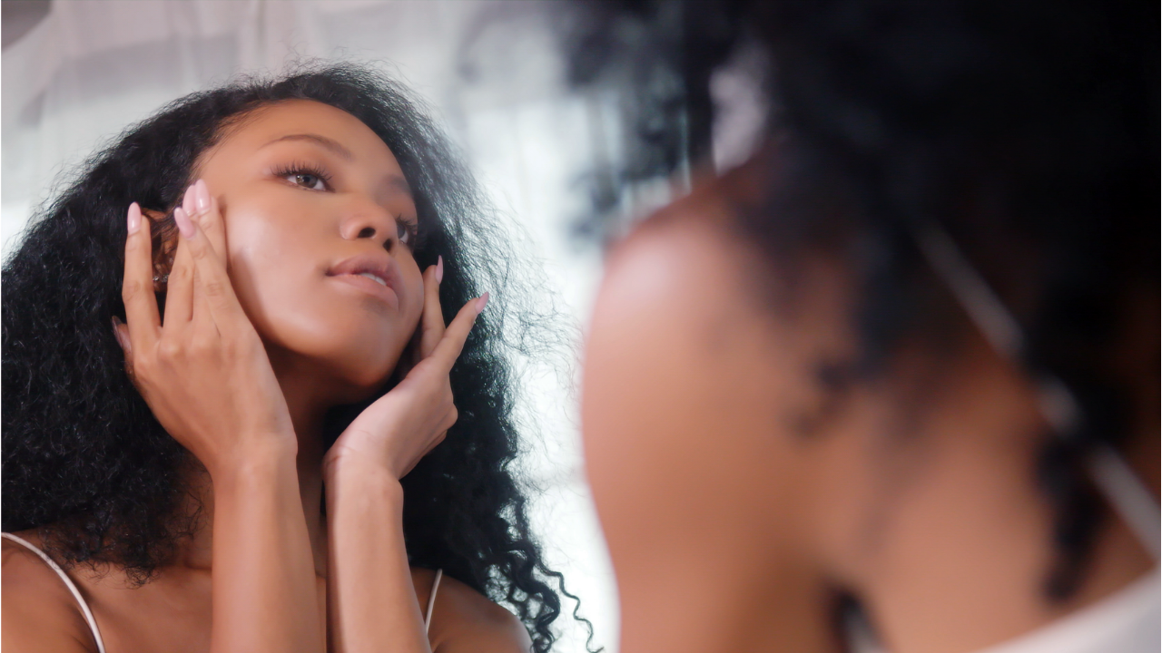 Une femme se regarde dans le miroir et effleure son visage du bout des doigts.