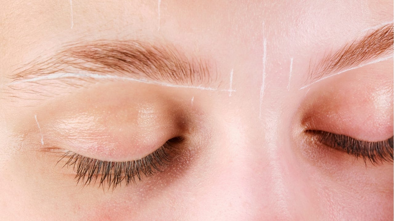 A close-up of a woman’s closed eyes and eyebrows, marked with white mapping lines for precise eyebrow shaping.