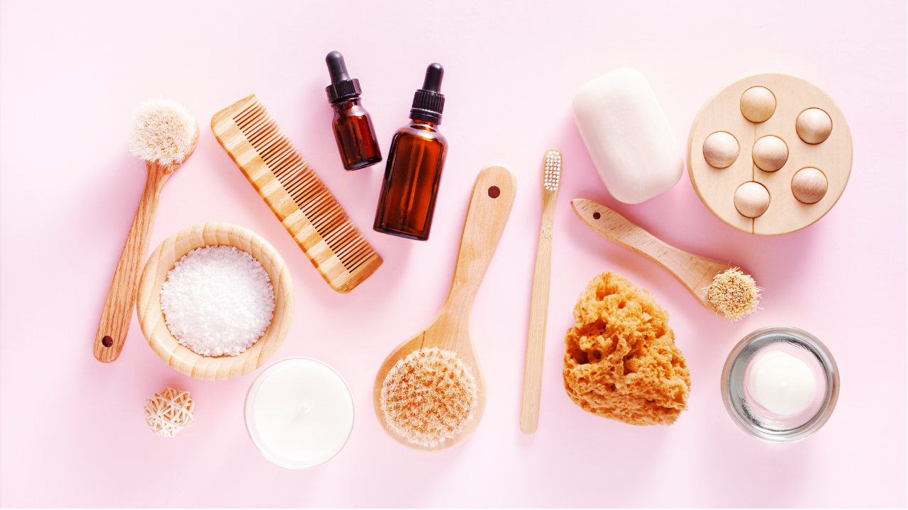A neatly arranged assortment of spa essentials, including brushes, oils, and sea salt, on a pink surface.