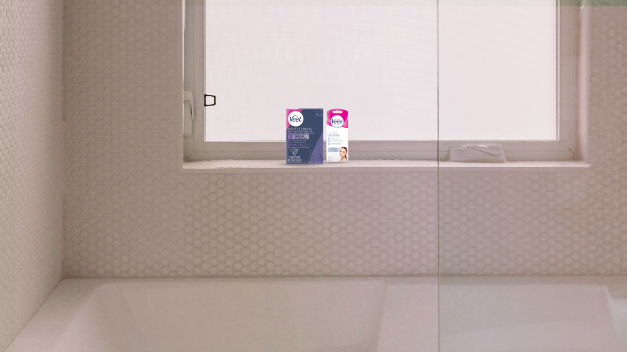Une salle de bains minimaliste avec une baignoire blanche épurée et un rebord de fenêtre sur lequel sont placés deux produits dépilatoires Veet.