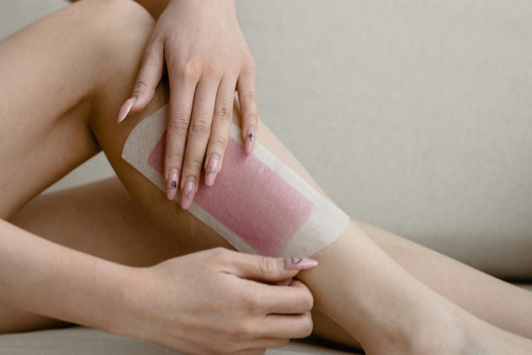 Une femme aux ongles roses applique une bande de cire sur sa jambe.