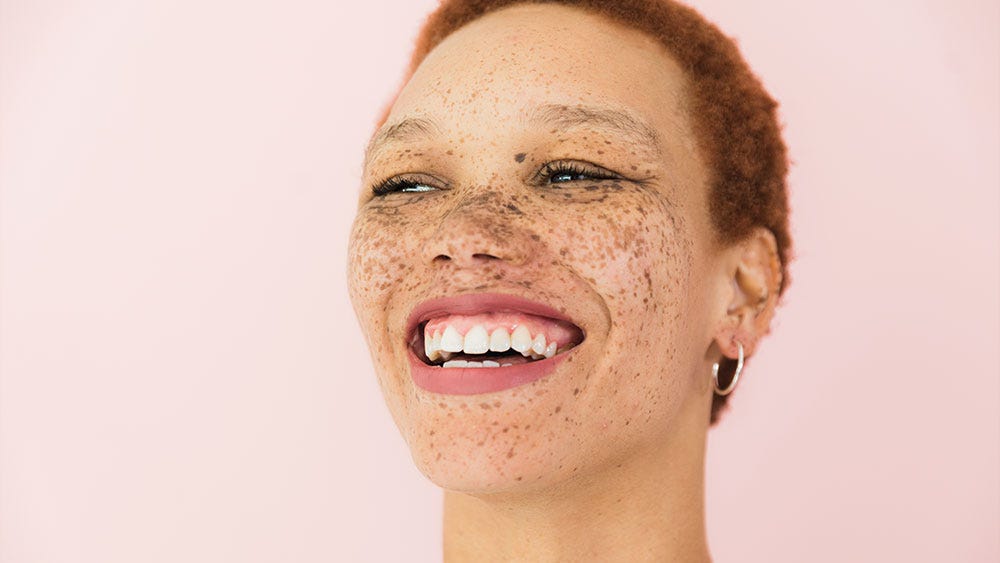 The face of a beautiful woman with very short reddish hair and lots of freckles looking happy with a huge smile.