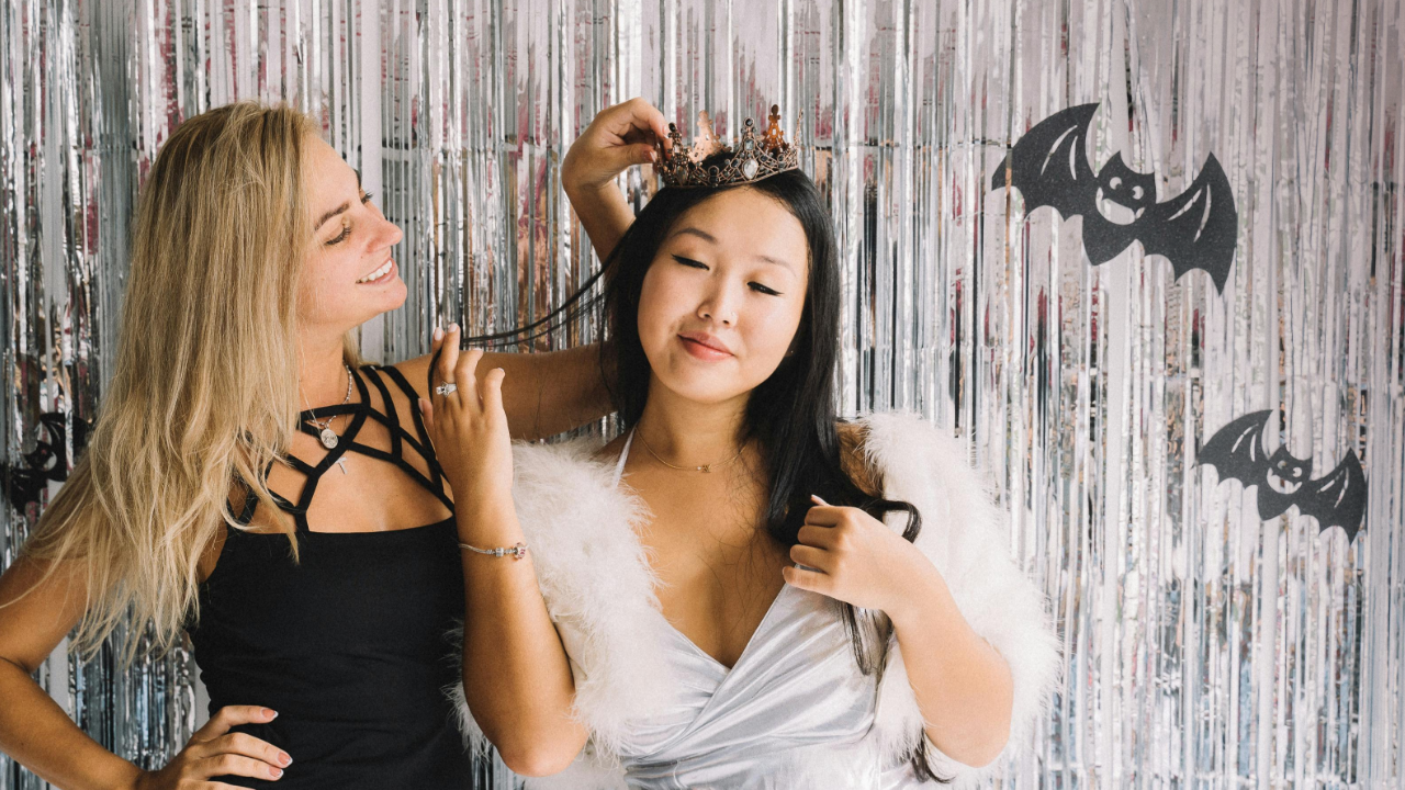 Une image de deux femmes en costume d’Halloween, entourées de décorations festives, sous un texte disant « Célébrez l’Halloween avec une peau lisse. »