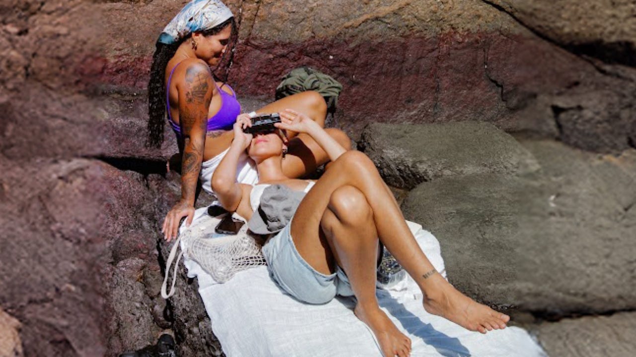 Two girls are sitting on a blanket on some rocks in the sunshine.