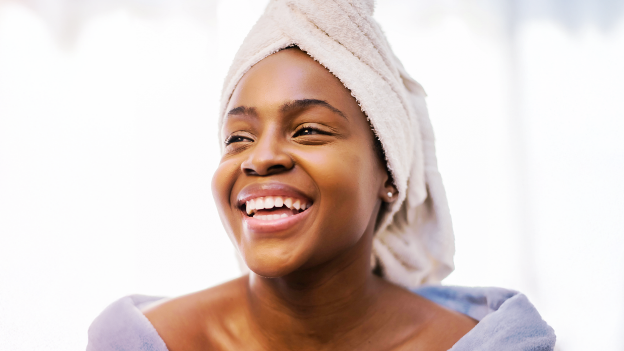 Smiling woman with a towel wrapped around her head, wearing a cozy robe.