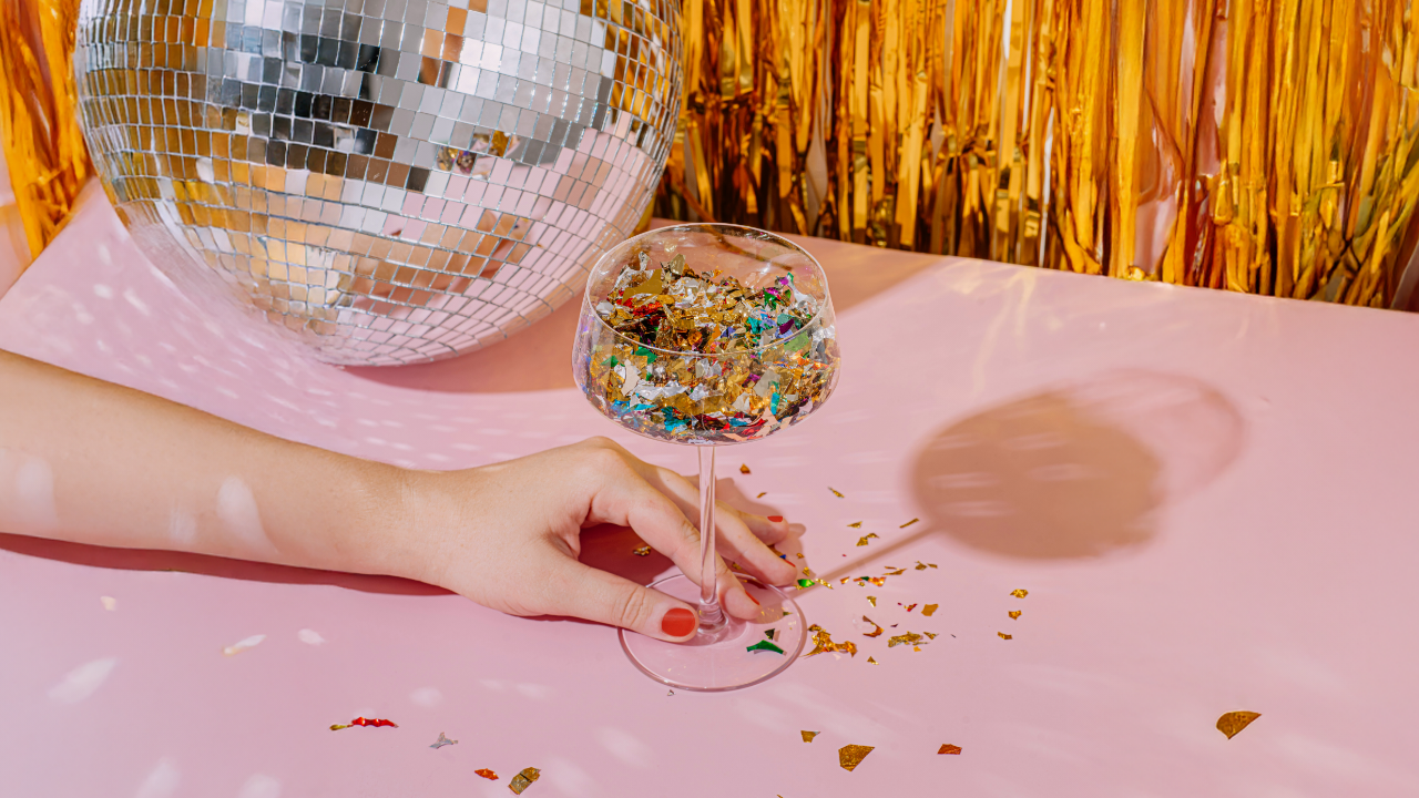 Une main tenant un verre rempli de confettis à côté d’une boule disco.