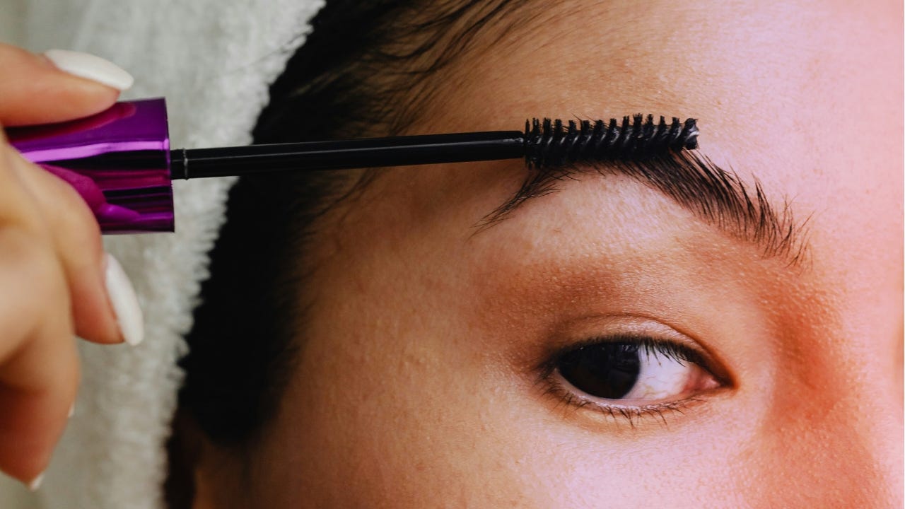 A close-up of a woman brushing their eyebrow with a spoolie.