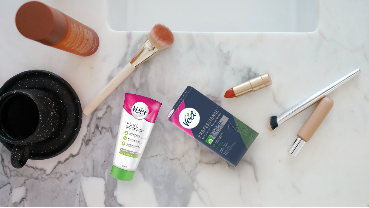 Veet and make-up products are laid out on a marble bathroom countertop.