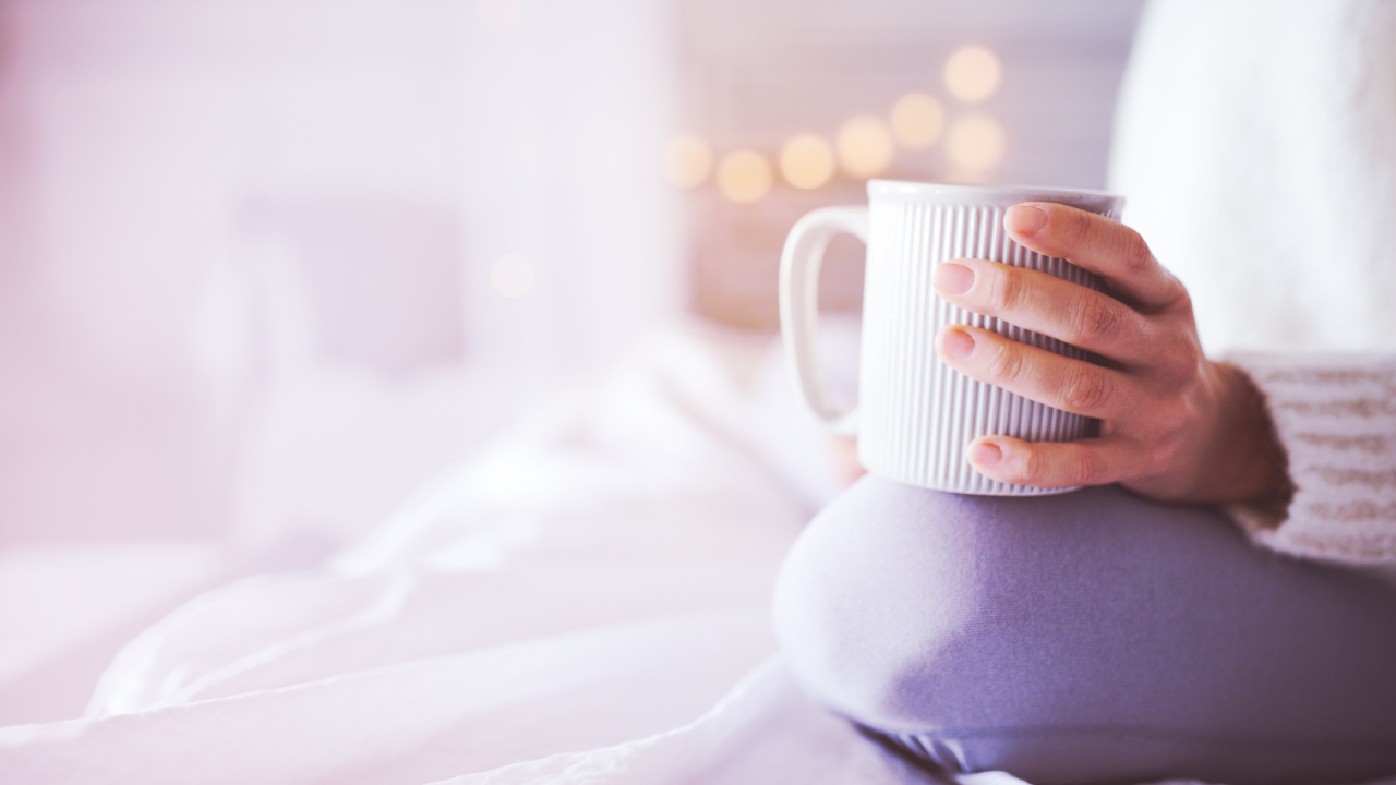 Une femme est assise sur son lit et tient une tasse de café.