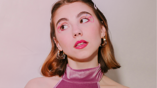 Une femme aux cheveux mi-longs portant du traceur pour les yeux rose vif semble réfléchir, le tout, sur un fond neutre.