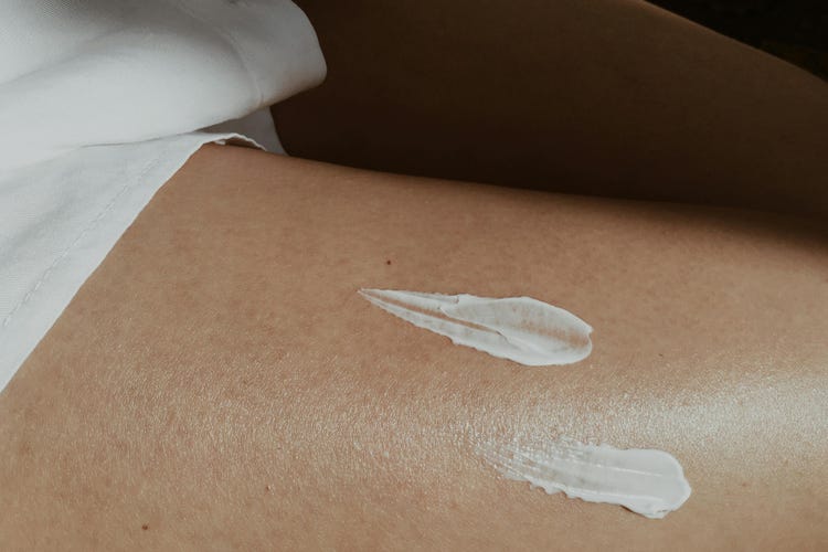 A close-up of two blots of lotion are smeared on a woman’s smooth thigh.