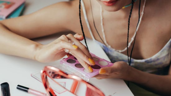 Une femme est assise à son comptoir de maquillage devant différents produits et un miroir.