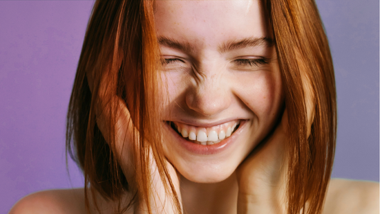 Gros plan d’une femme qui tient son visage dans ses mains, les yeux fermés, arborant un large sourire.