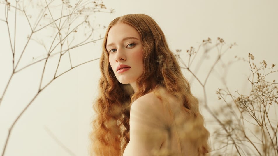Beautiful woman with porcelain skin and long red wavy hair looking over her bare shoulder at the camera.