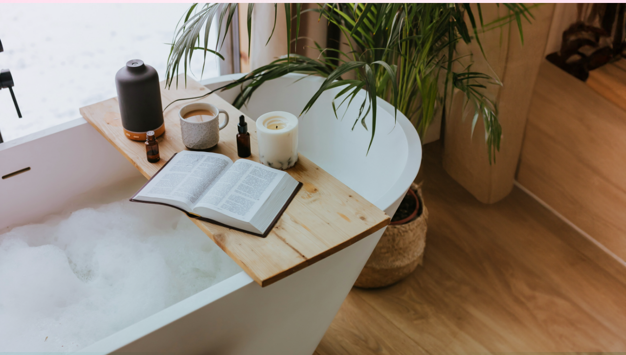Image d’un bain de mousse avec une bougie, un journal ouvert et une tasse de café sur le plateau de bain.