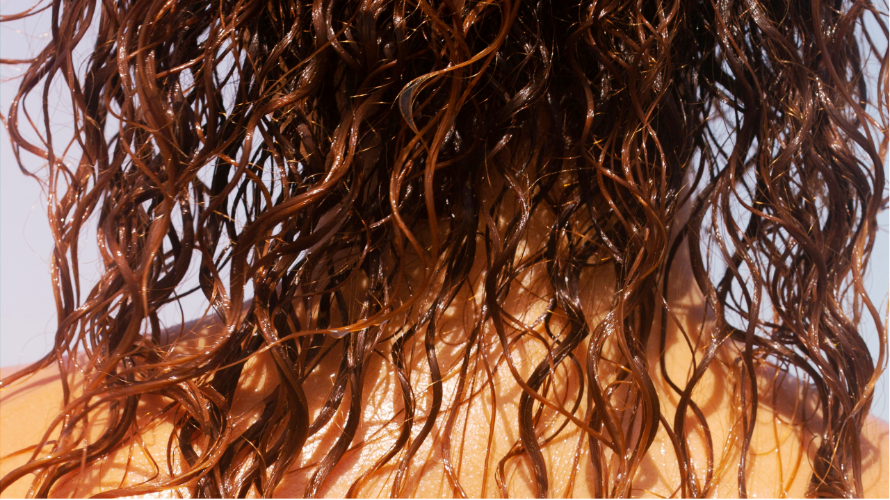 Gros plan de la tête d’une femme au sortir de la douche, dont les cheveux bruns et frisés sont mouillés.