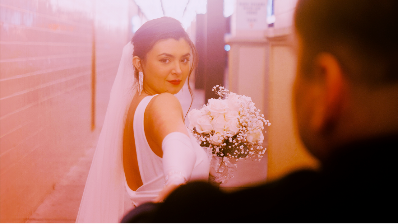 A bride in white dress holding a bouquet, looks back at her groom.