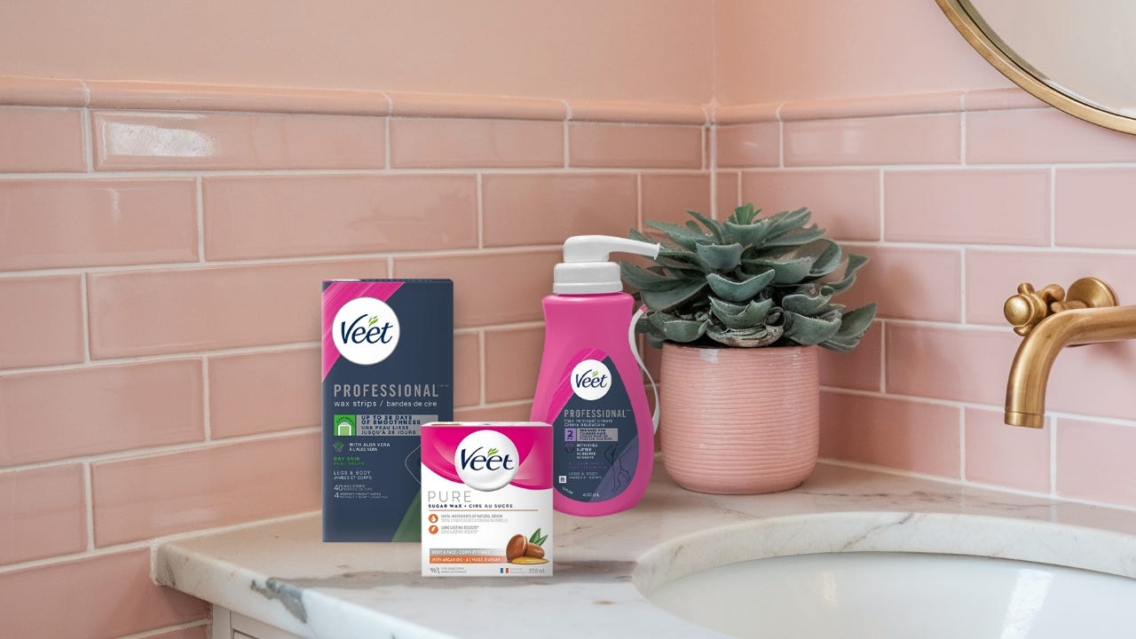 Veet Professional Wax Strips, Veet Professional Hair Removal Cream, and Veet PURE Sugar Wax Kit are displayed on a marble bathroom counter with pink tiles and a potted succulent.