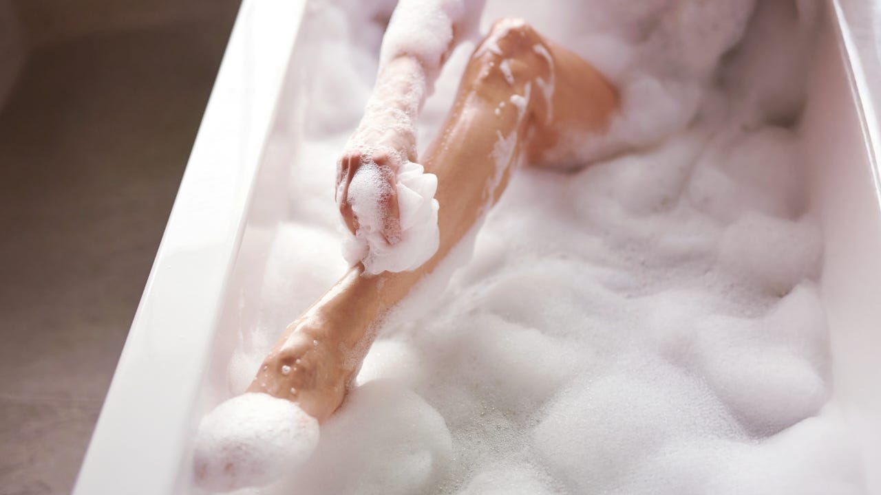 A close-up of a woman's bare leg covered in bubbles in the bathtub.