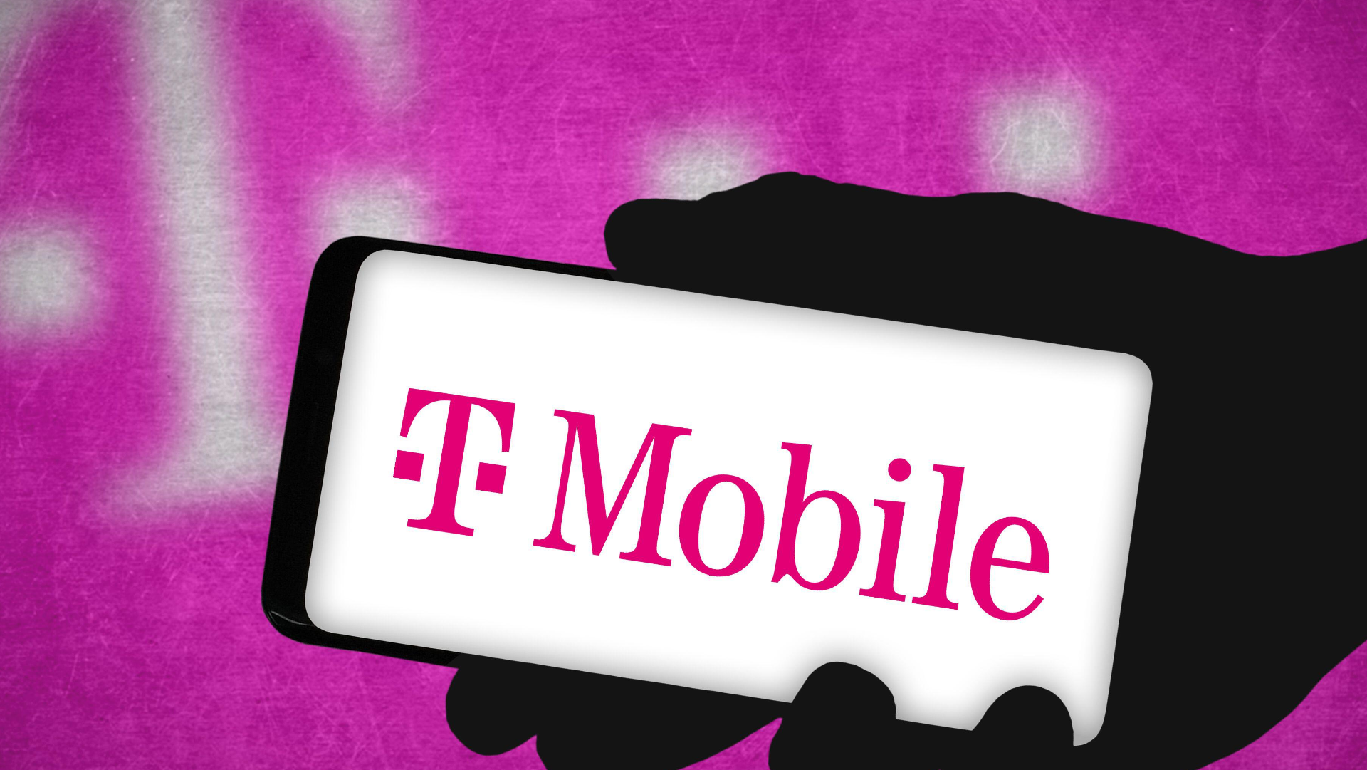 T-Mobile brand logo on a mobile device in a person's hand against a pink backdrop with the T-Mobile logo