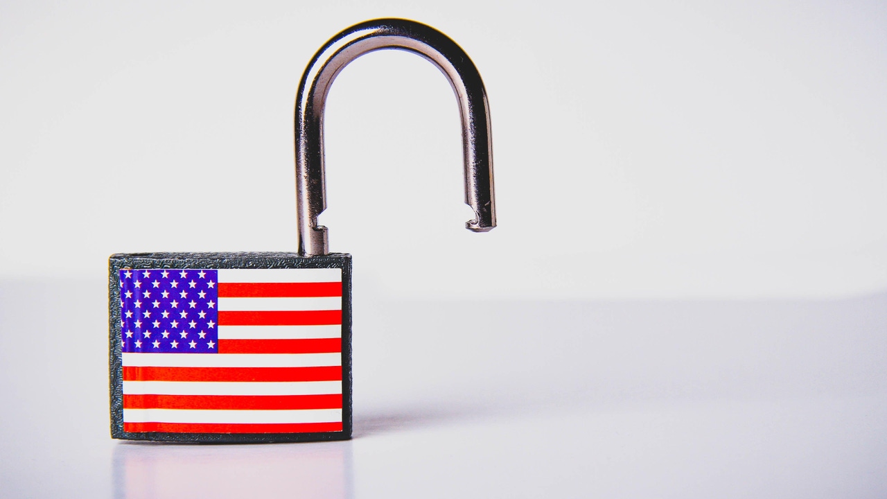 An open padlock with a USA flag on it sitting on a table An open padlock with a USA flag on it sitting on a table
