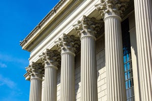 Photo of the tops of pillars on a government building, against a blue sky 