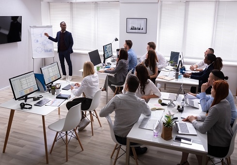 a person standing in the front of the room with a whiteboard and people sitting at their desks listening