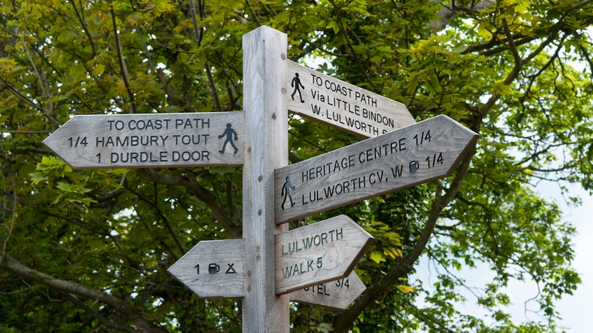 Wooden signpost shows directions to walking paths around West Lulworth, Dorset, England