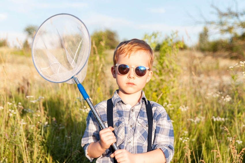 Photo of young boy in a field wearing sunglasses and holding a net ready to catch bugs.