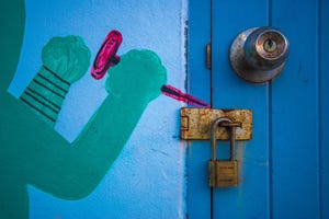 A painting on a wall of a green hand using a red tool to break a real lock on a door