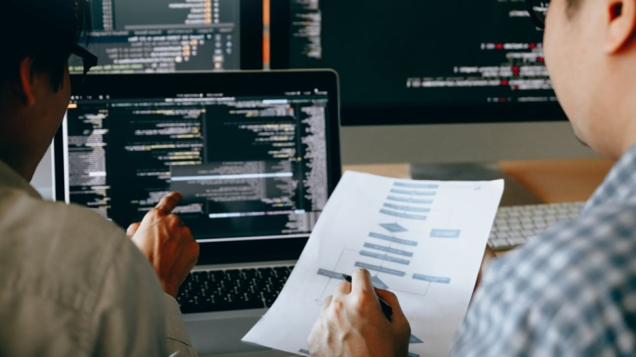 Two people looking at something on paper and on the screen. The text is blurry. Two people looking at something on paper and on the screen. The text is blurry.