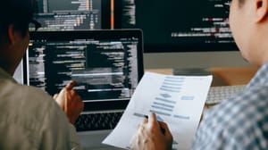 Two people looking at something on paper and on the screen. The text is blurry. Two people looking at something on paper and on the screen. The text is blurry.