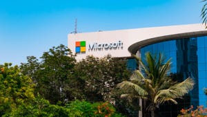 A white modern building with the Microsoft logo on the front, with trees covering the building A white modern building with the Microsoft logo on the front, with trees covering the building