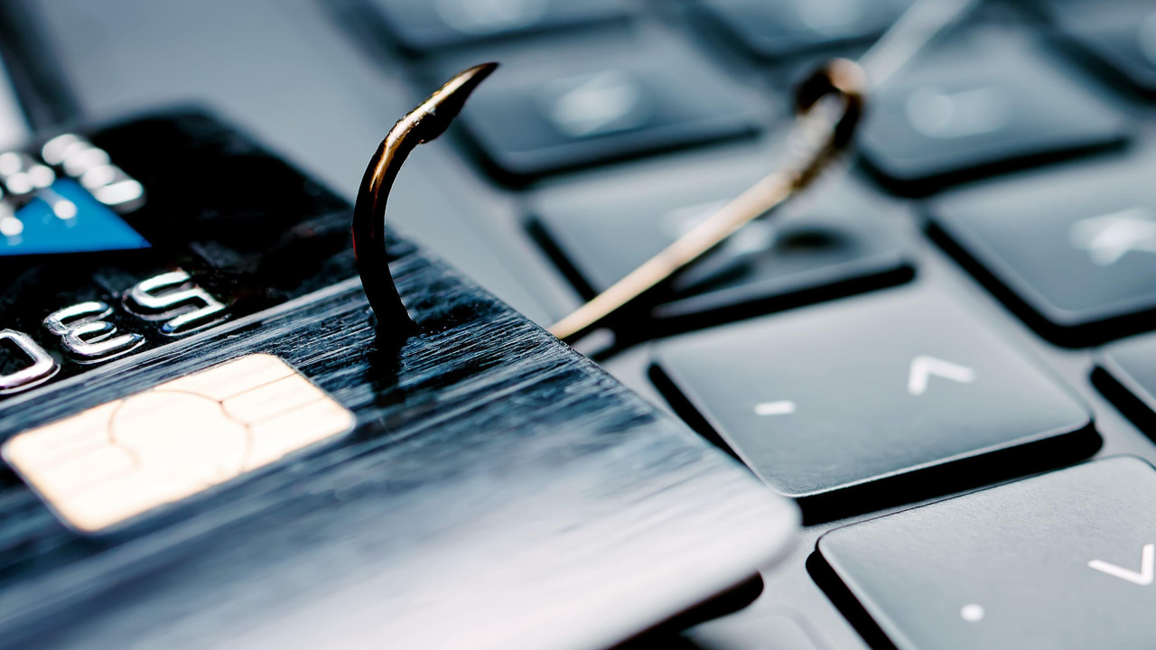 Credit card on top of a computer keyboard with a fish hook in it Credit card on top of a computer keyboard with a fish hook in it