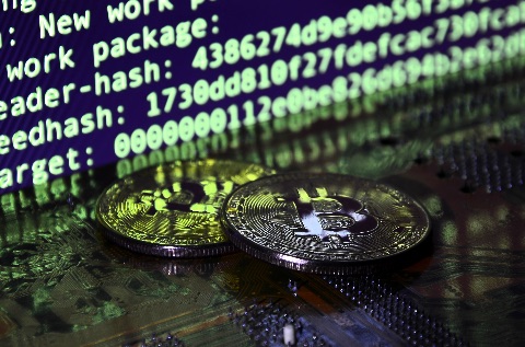 coins marked with 'B' for bitcoin in front of a computer screen showing the ledger.