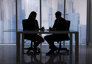Silhouettes of two people sitting at a table talking.