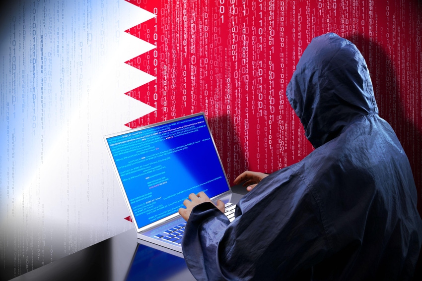 A person in a hoodie using a laptop in front of the Qatar flag