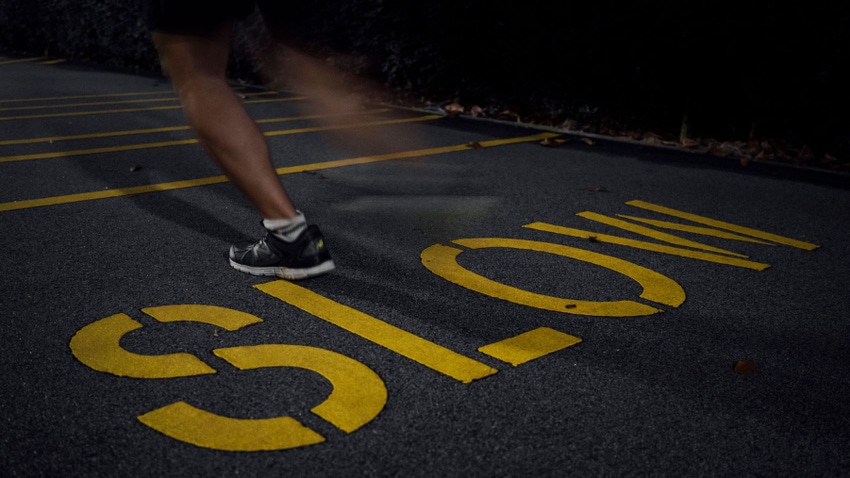 Legs of a person seen running over the word SLOW on blacktop