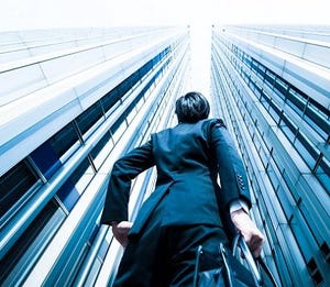 Person in a dark business suit holding a briefcase and looking up at two skyscrapers.
