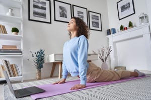 Fit young woman doing yoga stretching exercise on floor in front of open laptop.
