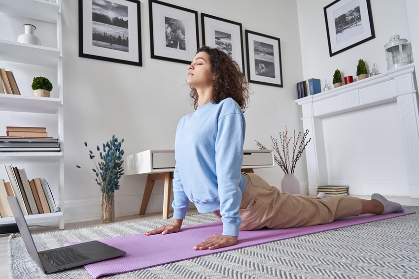 Fit young woman doing yoga stretching exercise on floor in front of open laptop.