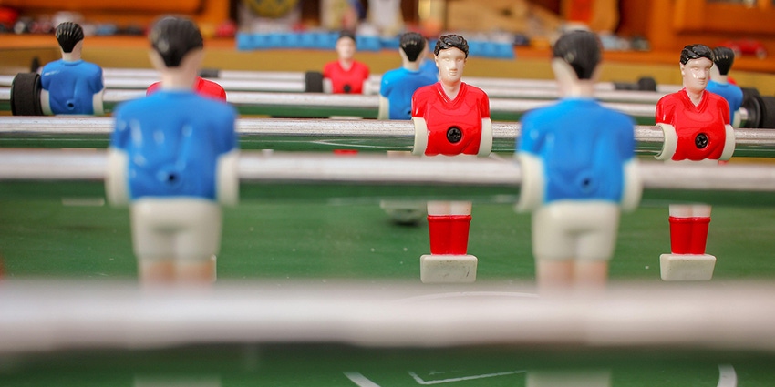 Photo of the figures on a foosball table, where you see the red team's faces and the blue team players are blurry
