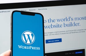 WordPress Logo on blue screen of a smartphone with WordPress homepage on the screen of a laptop in background