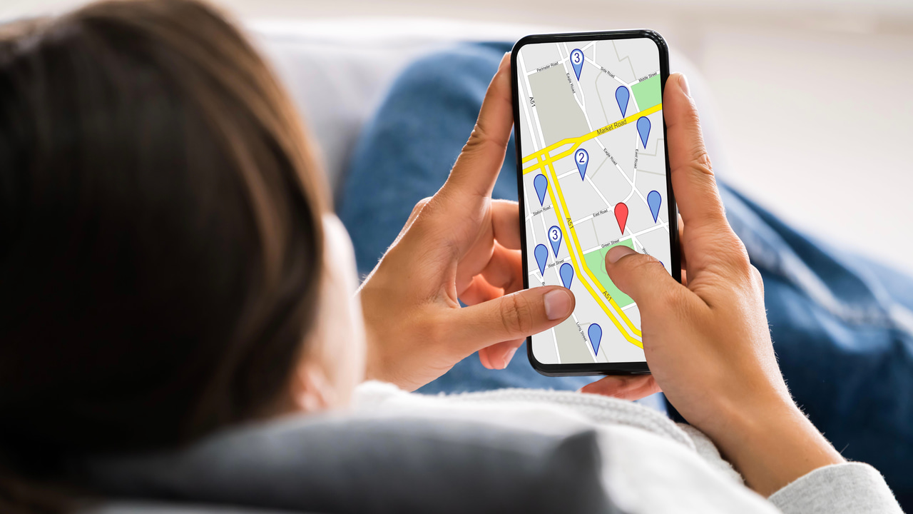 電話を持って横たわる女性。画面には地図上にピン留めされた場所が表示されている 電話を持って横たわる女性。画面には地図上にピン留めされた場所が表示されている