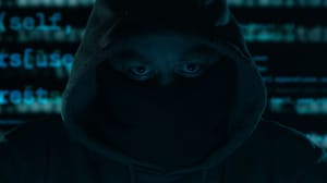 A hooded figure with a masked face, program code in the background in a dark setting A hooded figure with a masked face, program code in the background in a dark setting