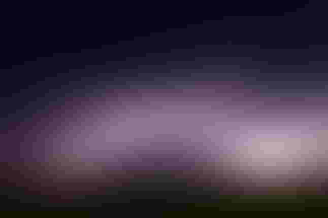 Image of a cloud burst on the horizon, with lightning lighting up a purple pile of clouds