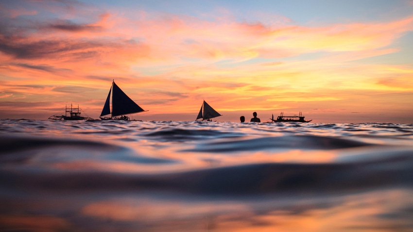 Silhouette of boats and people swimming at sunset, Phillipines