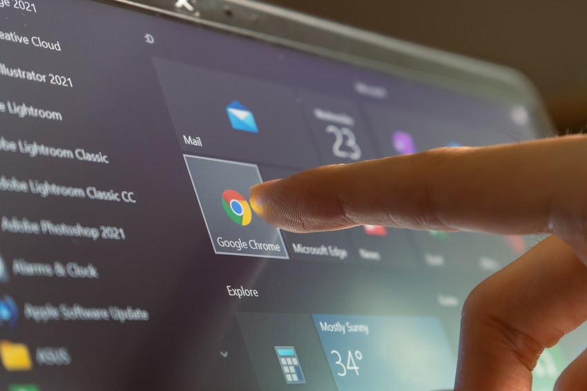 Finger touching Google Chrome icon on computer screen