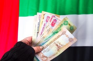 A hand holding UAE currency in front of the flag