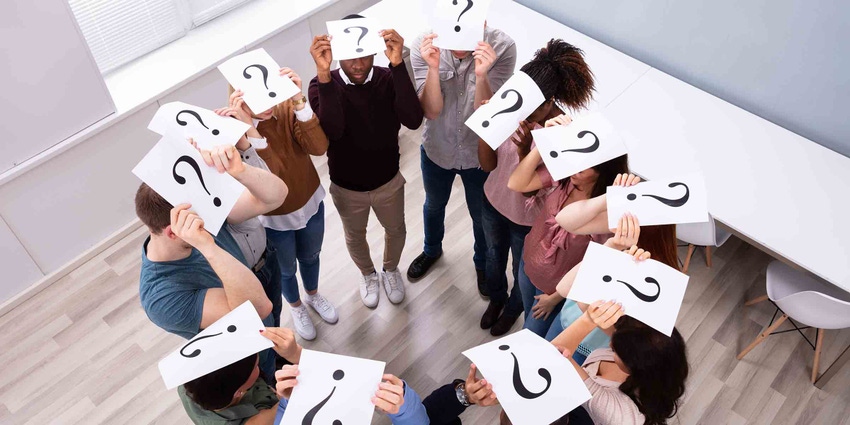 a group of co-workers standing in a circle holding a paper with a question mark over their heads.
